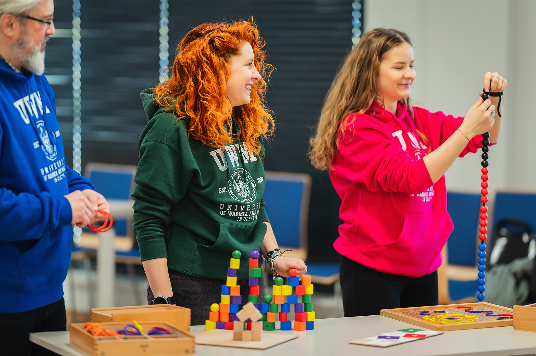 Trzy osoby pracują przy stole z pomocami edukacyjnymi