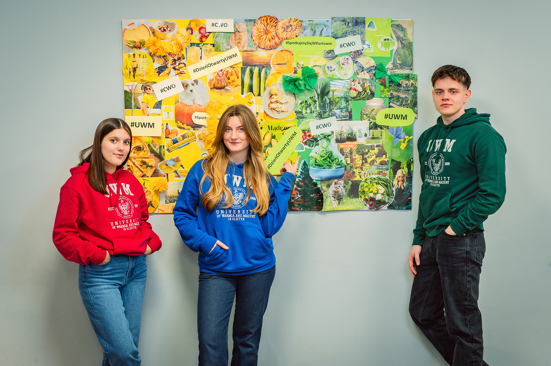 Troje studentów stoi przed kolorową tablicą z kolażem tematycznym