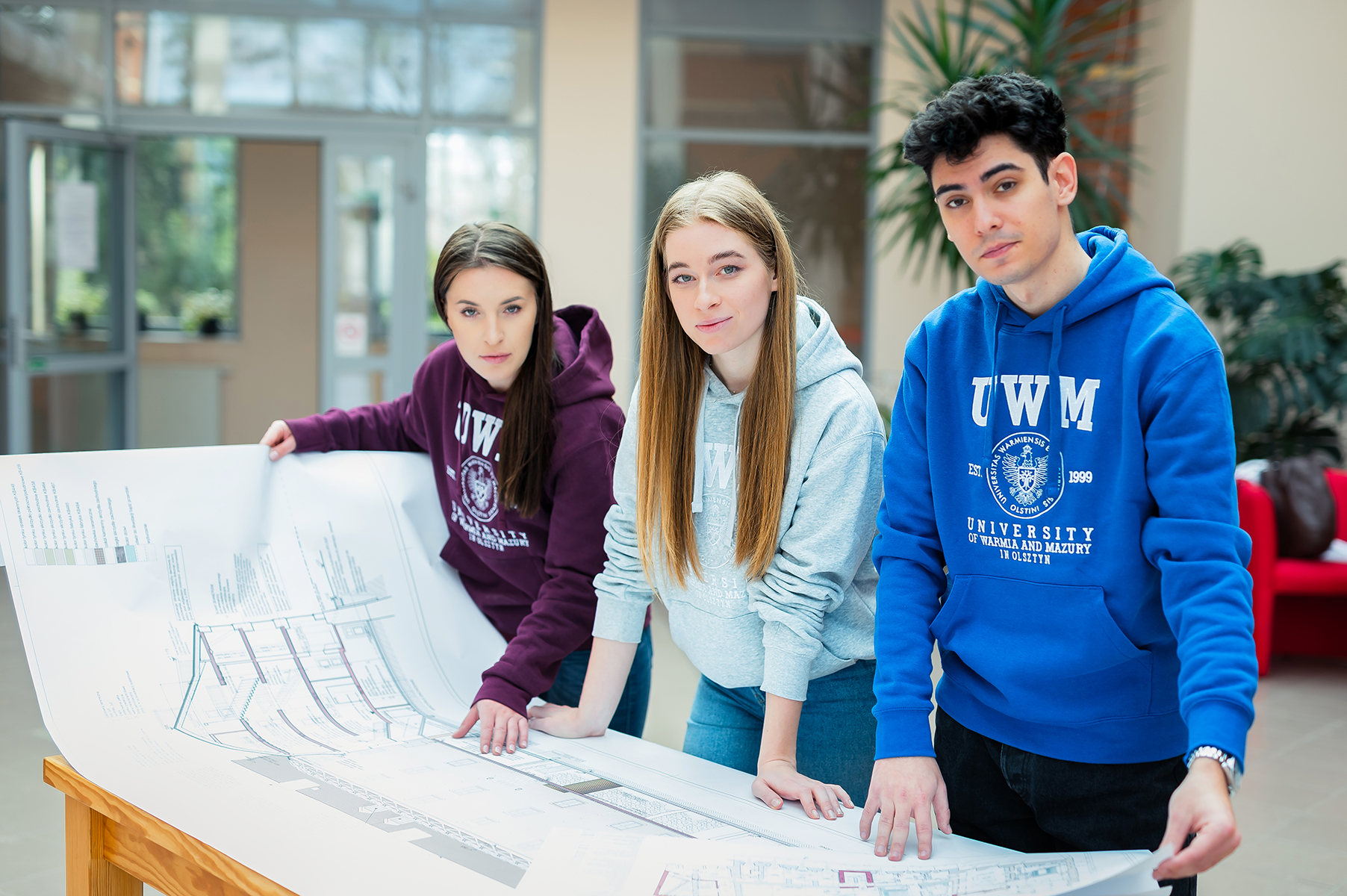Studenci w bluzach UWM przeglądający duże plany techniczne