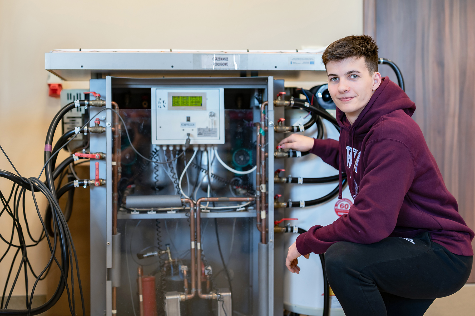 Osoba kuca przy urządzeniu laboratoryjnym i reguluje jego element