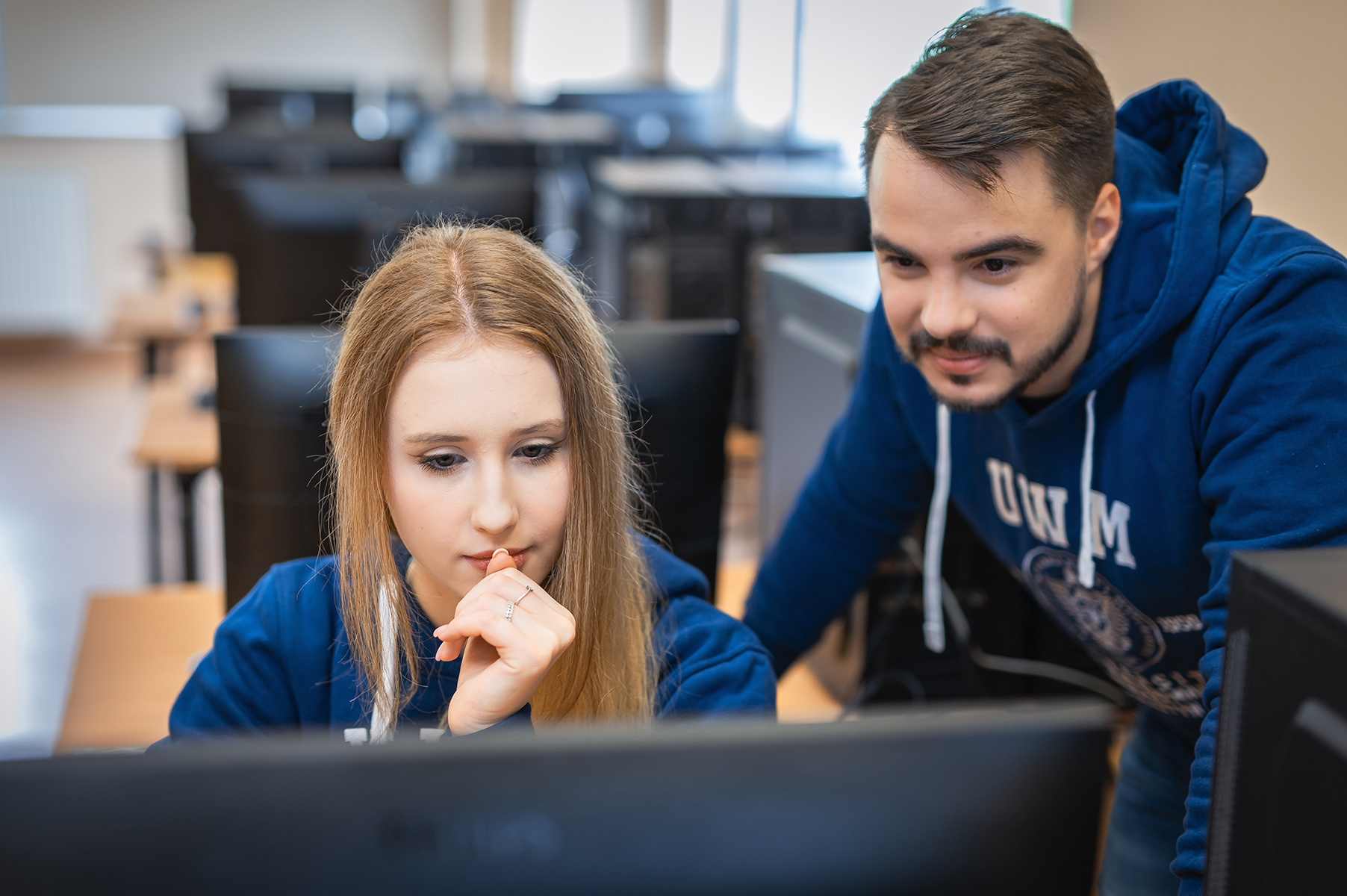 Studentka i student w bluzach UWM patrzą na ekran komputera