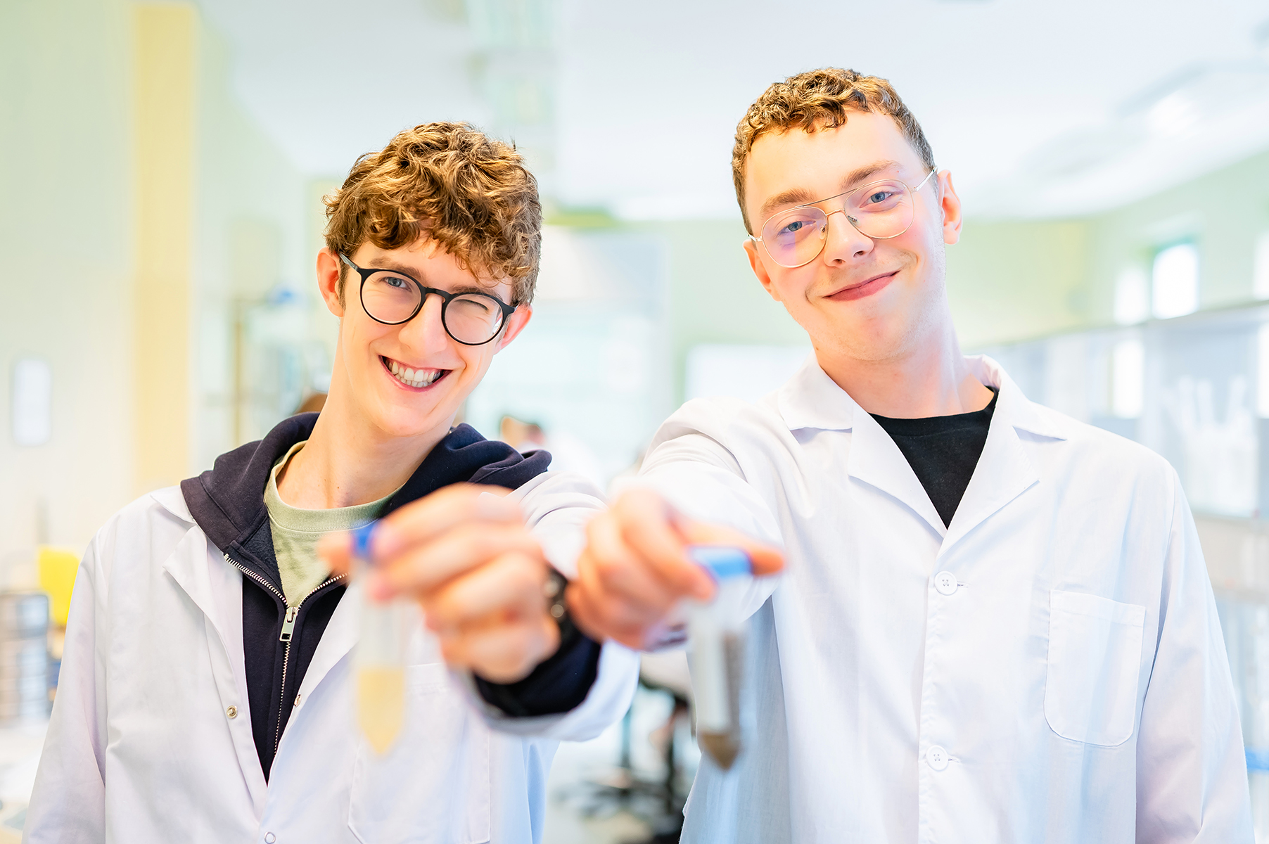 Studenci w fartuchach laboratoryjnych trzymają probówki z próbkami