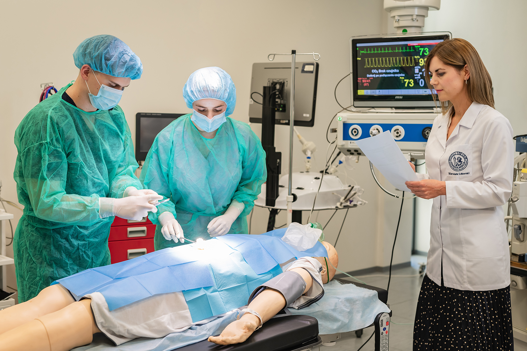 Studenci w strojach chirurgicznych przeprowadzający zabieg na fantomie medycznym pod okiem instruktorki