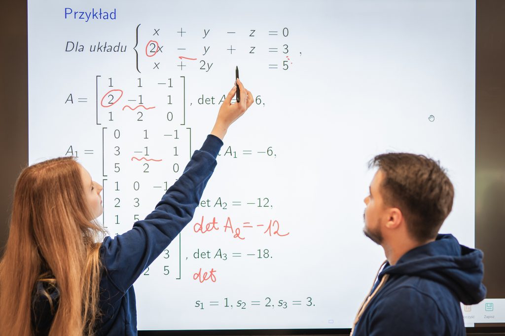 Dwoje studentów analizujących układy równań i macierze na tablicy interaktywnej
