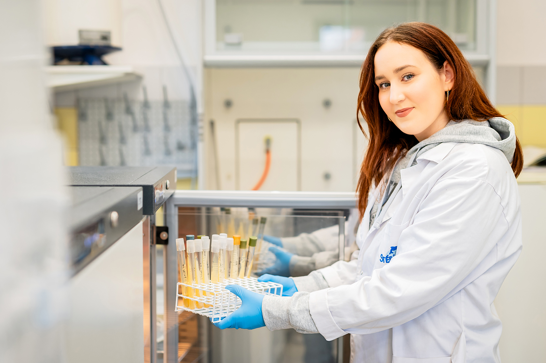 Studentka w laboratorium trzymająca statyw z probówkami przy urządzeniu chłodniczym