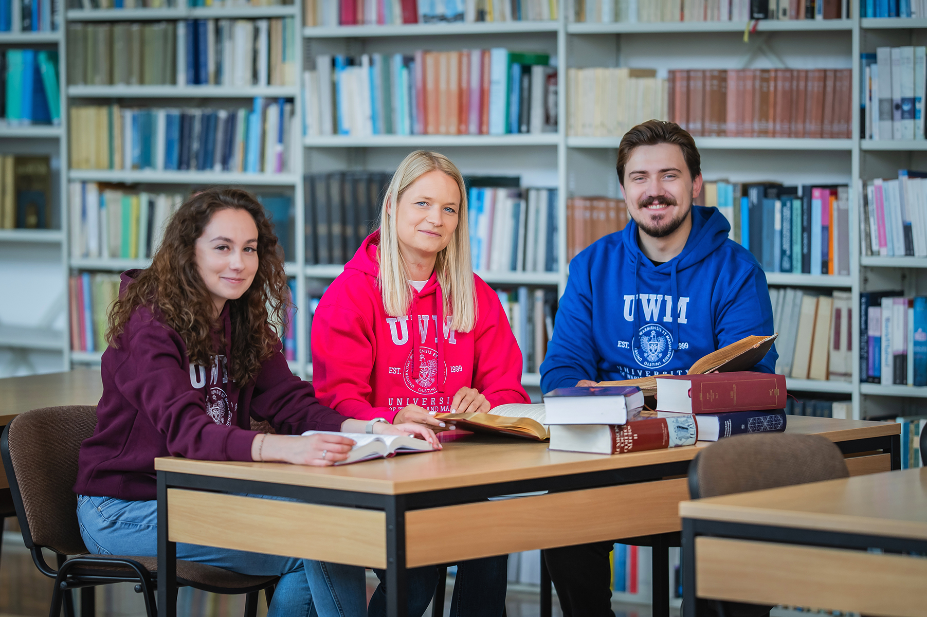 Trzy osoby siedzą przy stole w bibliotece i pracują z książkami