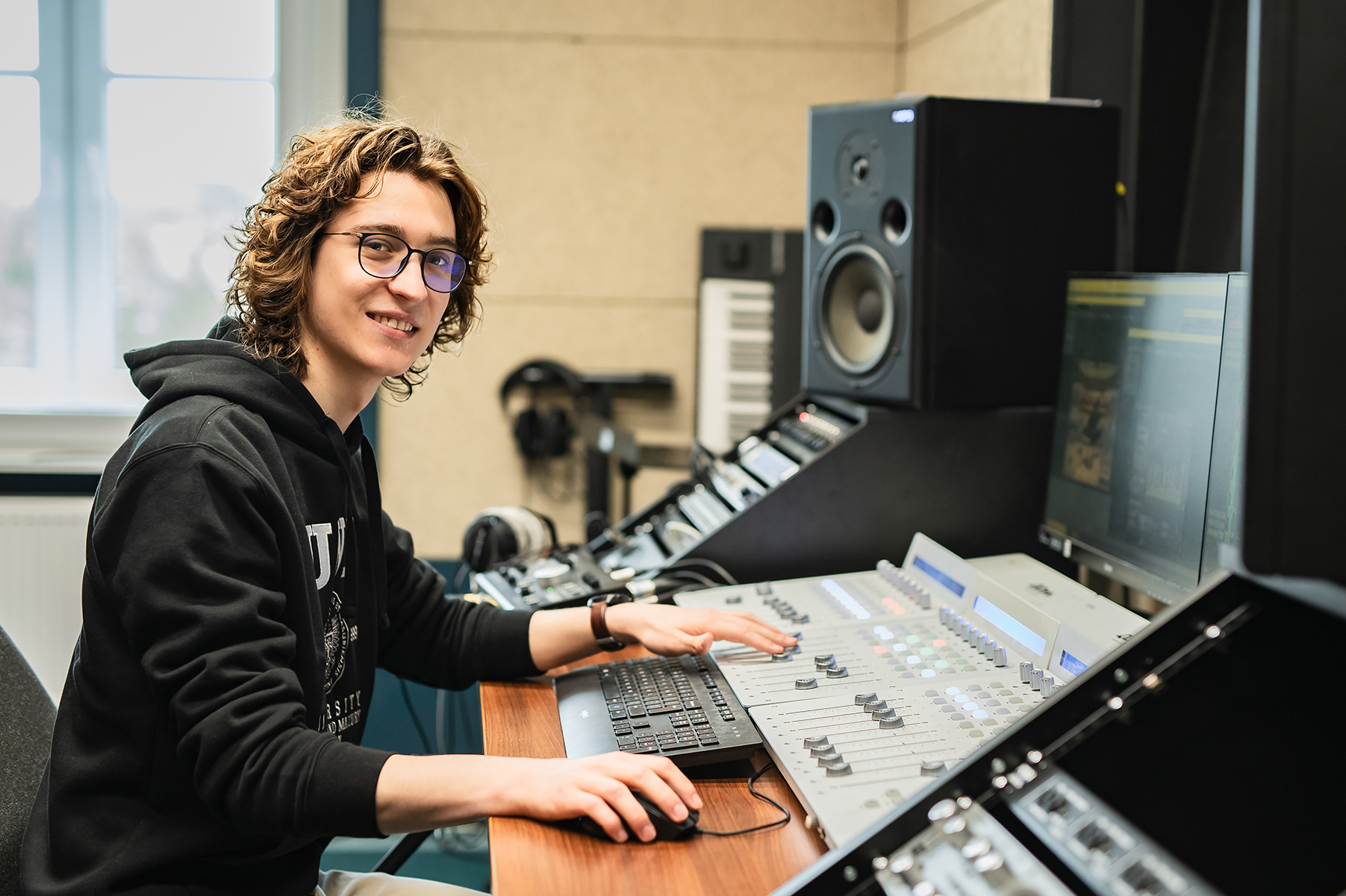 Osoba siedzi przy konsolecie dźwiękowej w studiu nagrań i obsługuje sprzęt audio