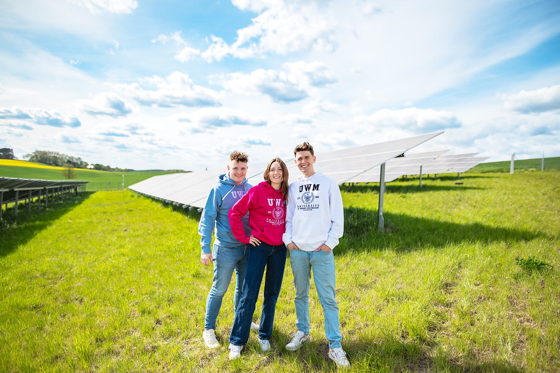 Trzy osoby stoją na trawiastym terenie przy instalacji paneli fotowoltaicznych