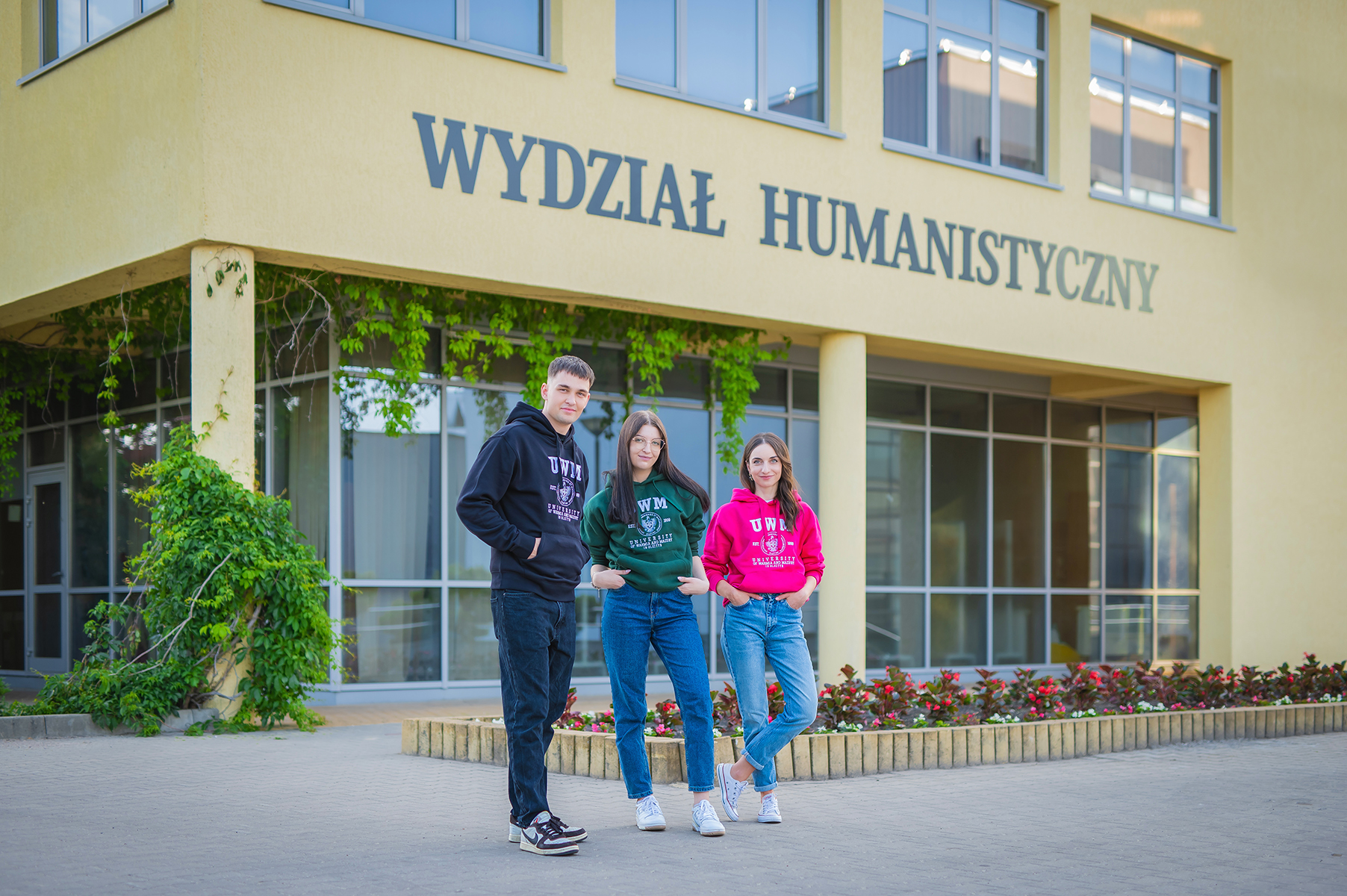 Studenci w bluzach UWM stoją przed wejściem do budynku Wydziału Humanistycznego