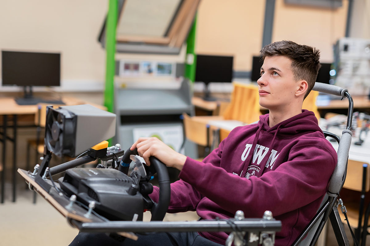 Student siedzi na stanowisku symulatora jazdy, trzyma kierownicę