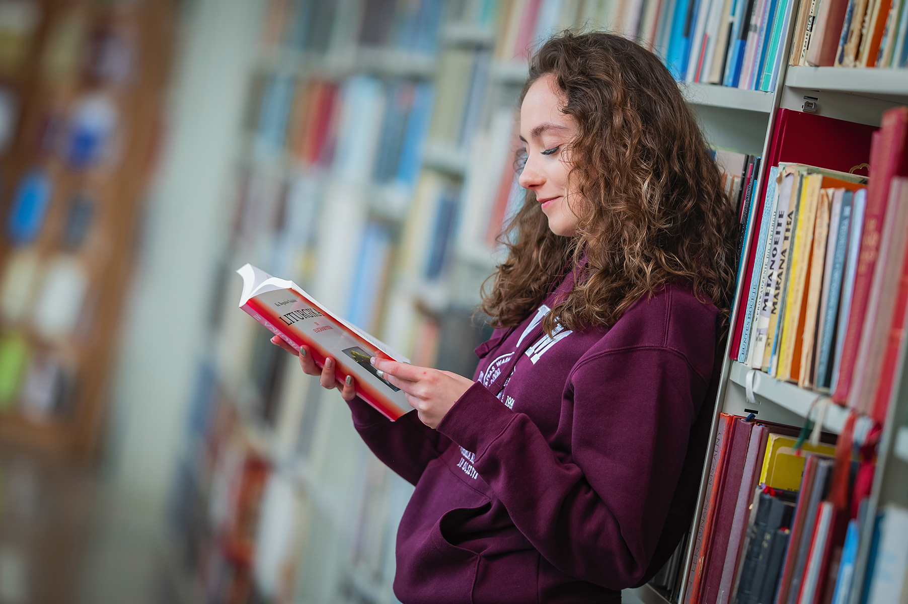 Osoba stoi przy regale bibliotecznym i czyta książkę