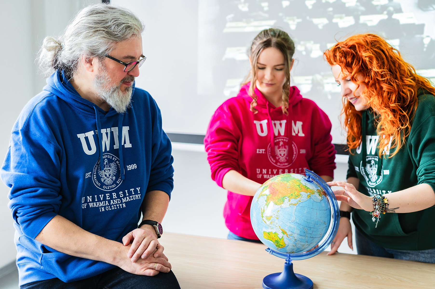 Trzy osoby oglądają globus stojący na stole w sali