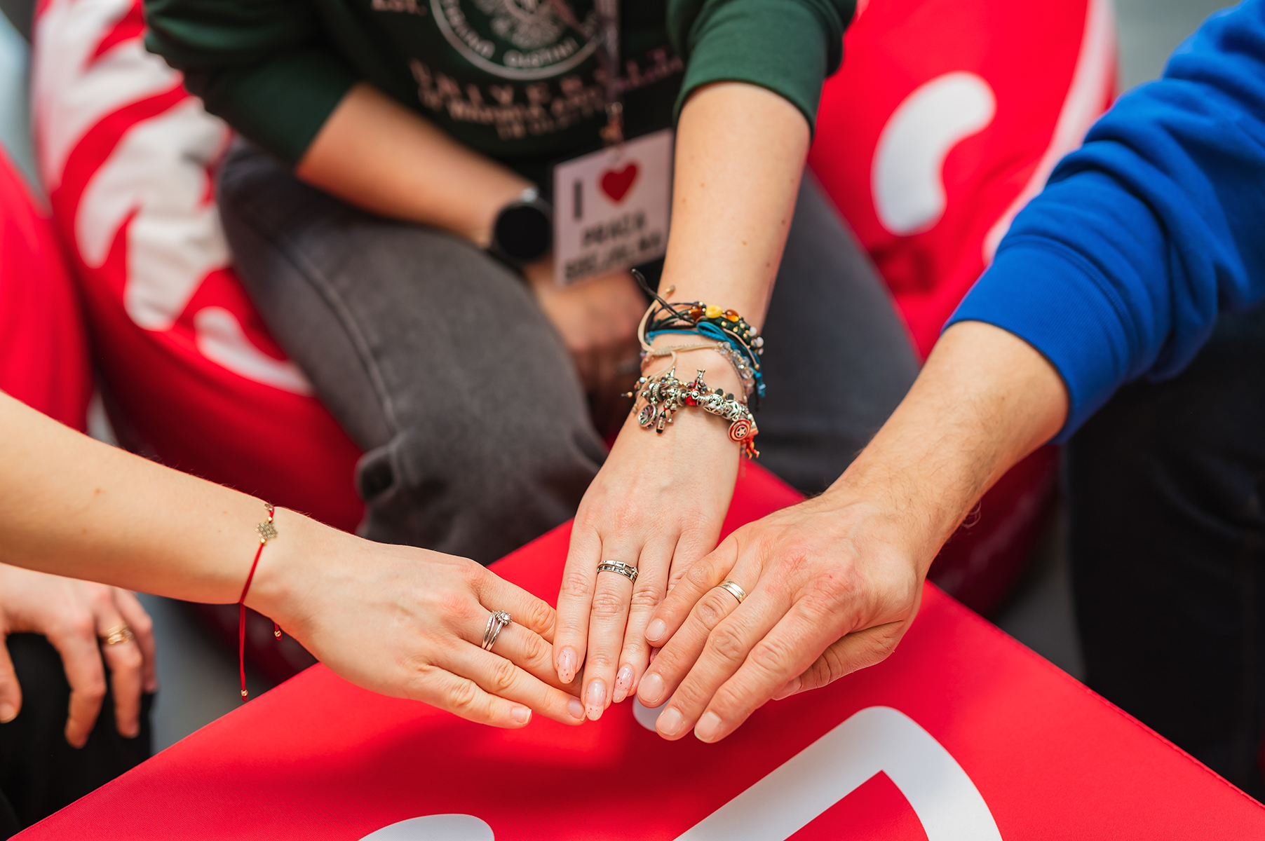 Dłonie kilku osób ułożone razem na czerwonym siedzisku