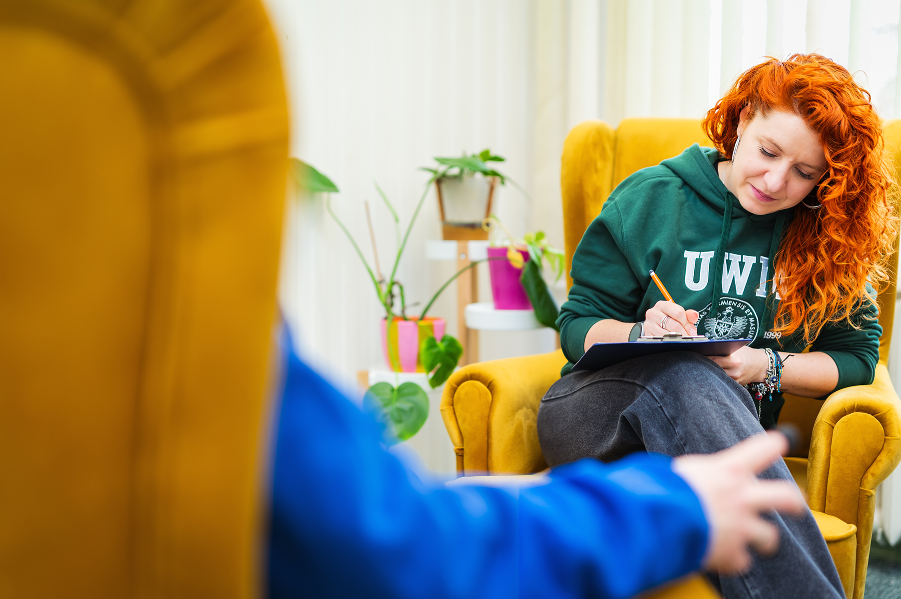 Osoba siedzi w fotelu i notuje na podkładce podczas rozmowy