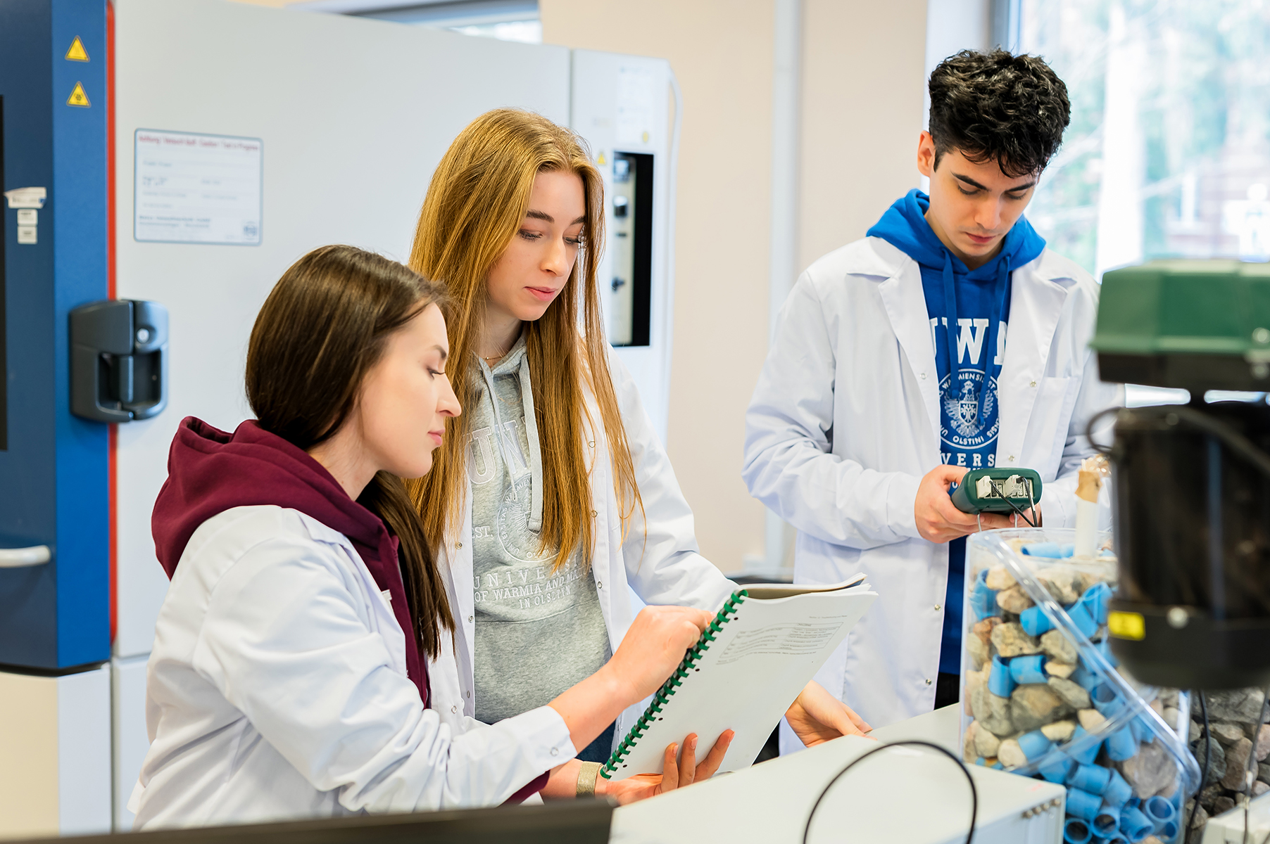 Studenci w laboratorium analizujący dokumentację i urządzenie pomiarowe