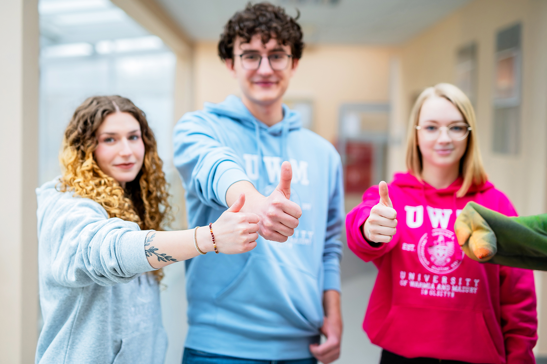 Troje studentów uśmiechających się i pokazujących gest kciuka w górę