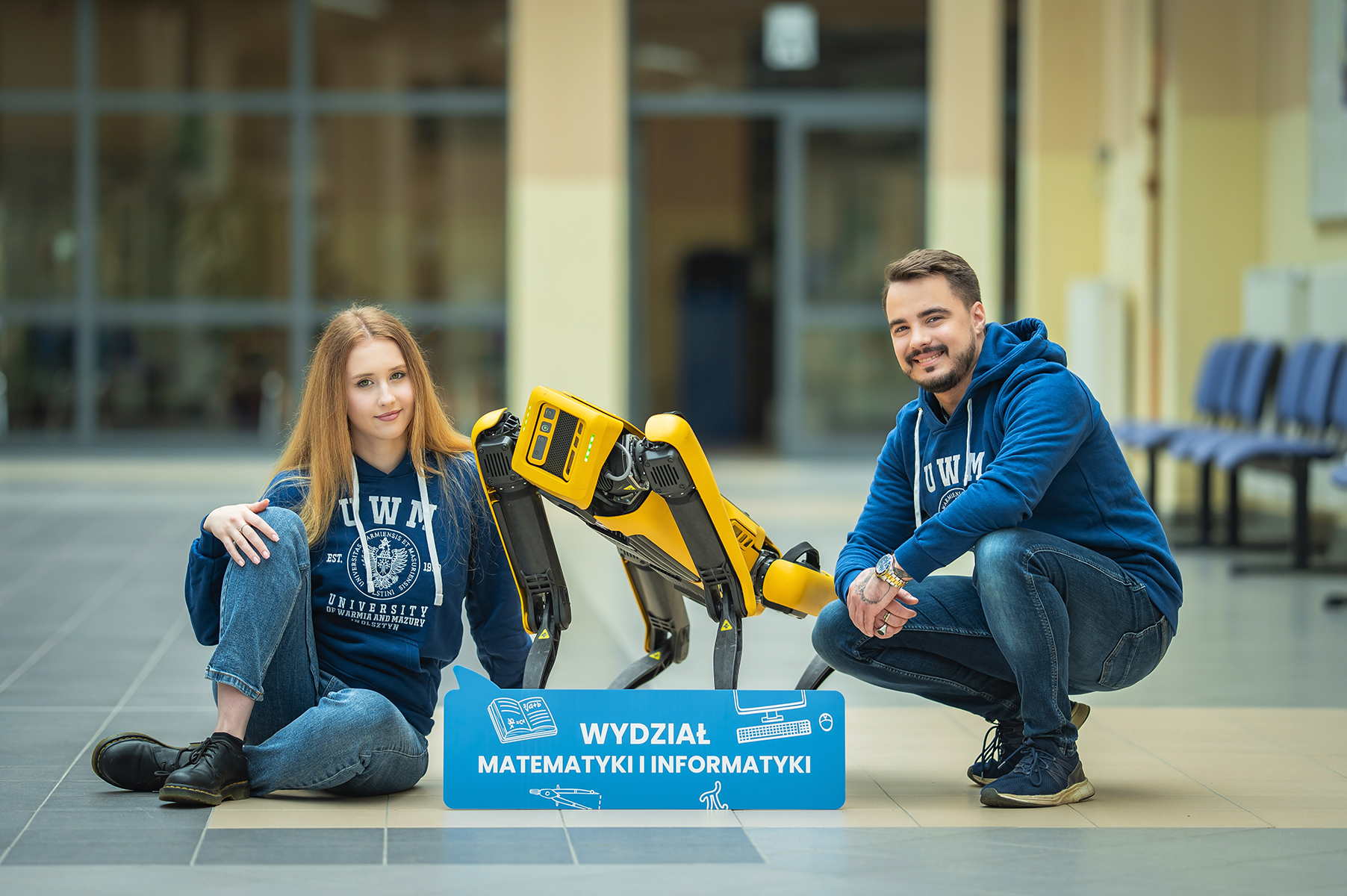 Studenci pozujący z żółtym psem robotycznym obok tabliczki Wydziału Matematyki i Informatyk