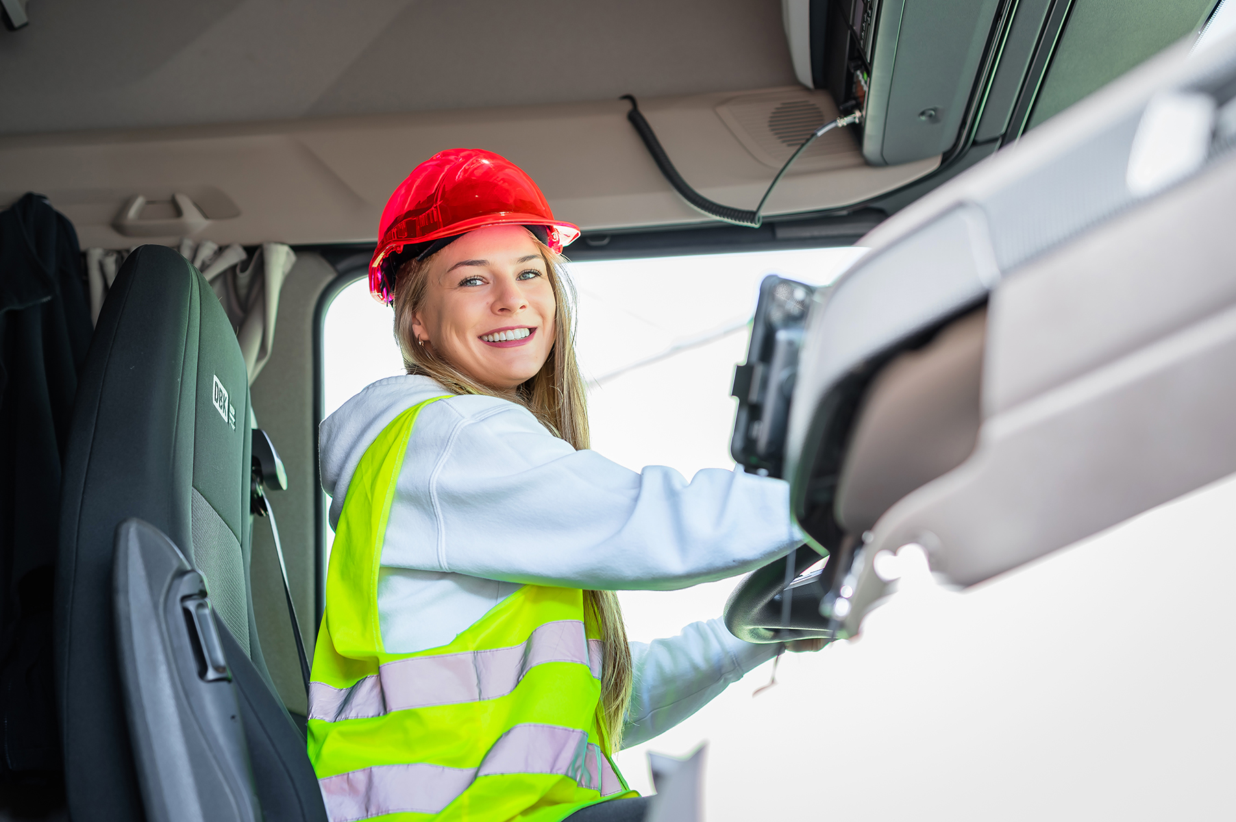 Kobieta w kasku i kamizelce odblaskowej siedząca za kierownicą ciężarówki