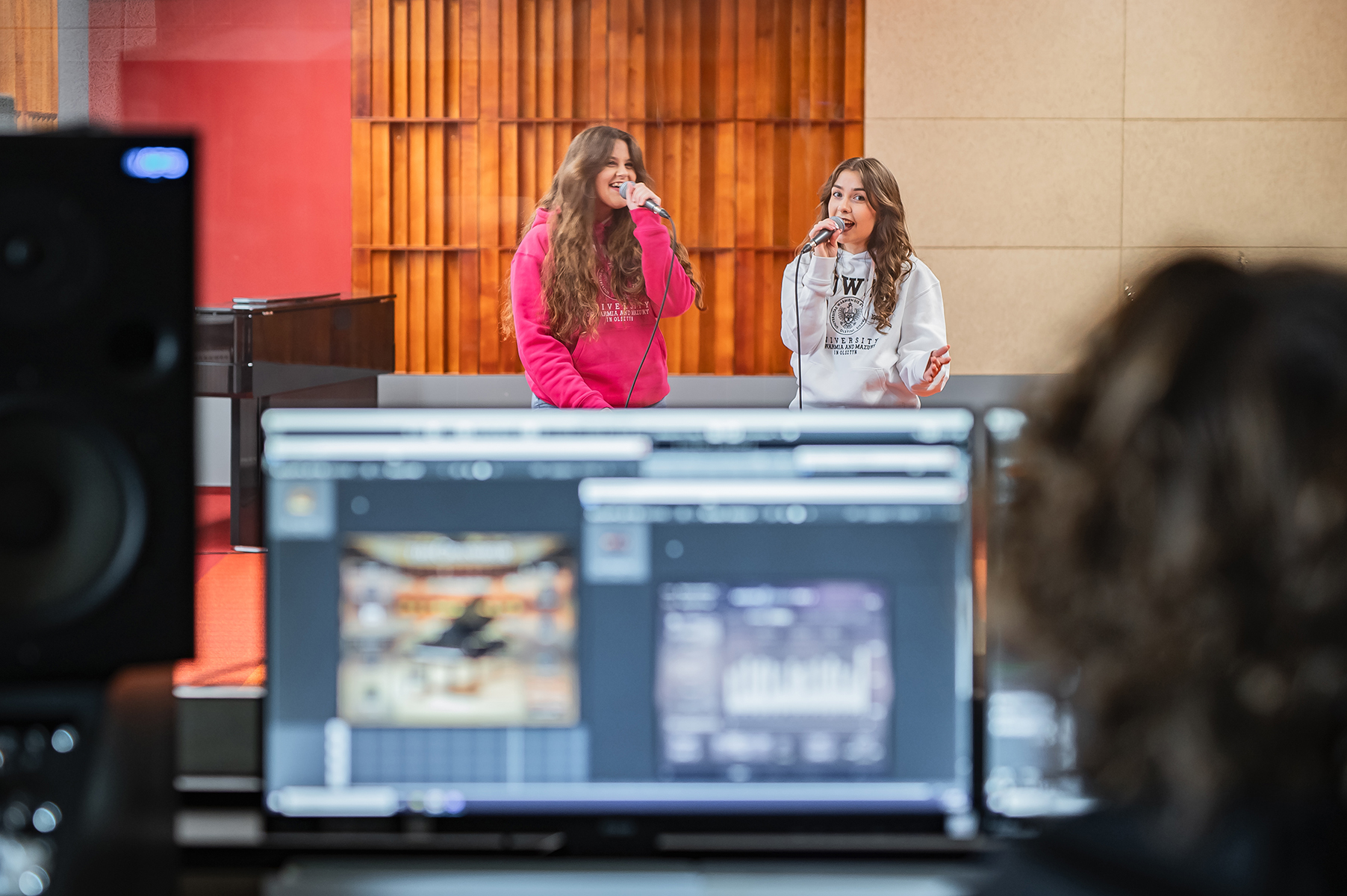 Dwie osoby śpiewają do mikrofonów w studiu nagrań, widok z reżyserki dźwięku