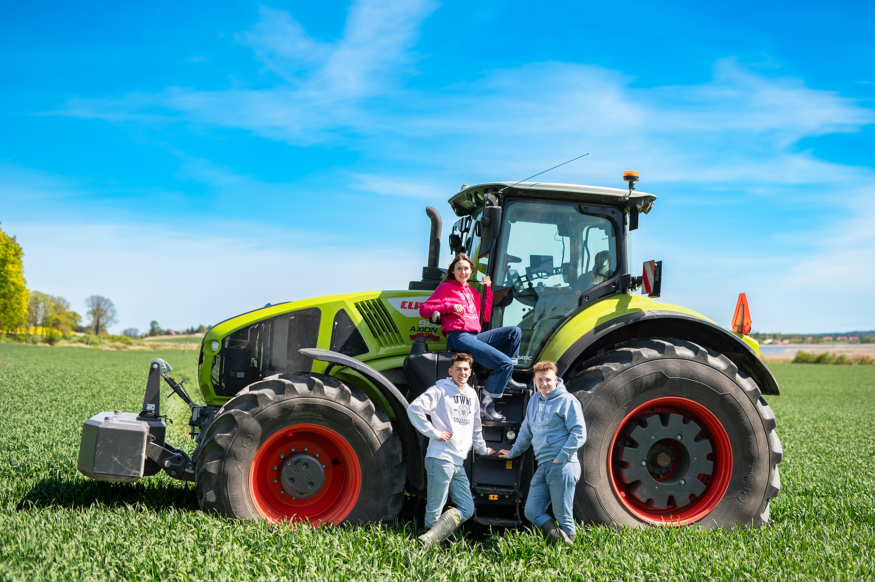 Trzy osoby stoją przy dużym ciągniku rolniczym na zielonym polu