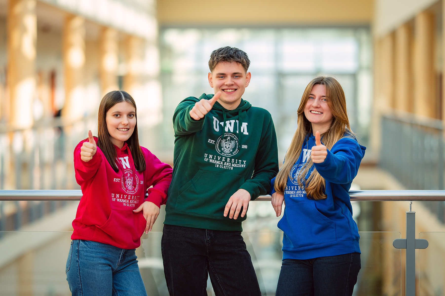 Uśmiechnięci studenci w kolorowych bluzach UWM pokazują gest kciuka w górę