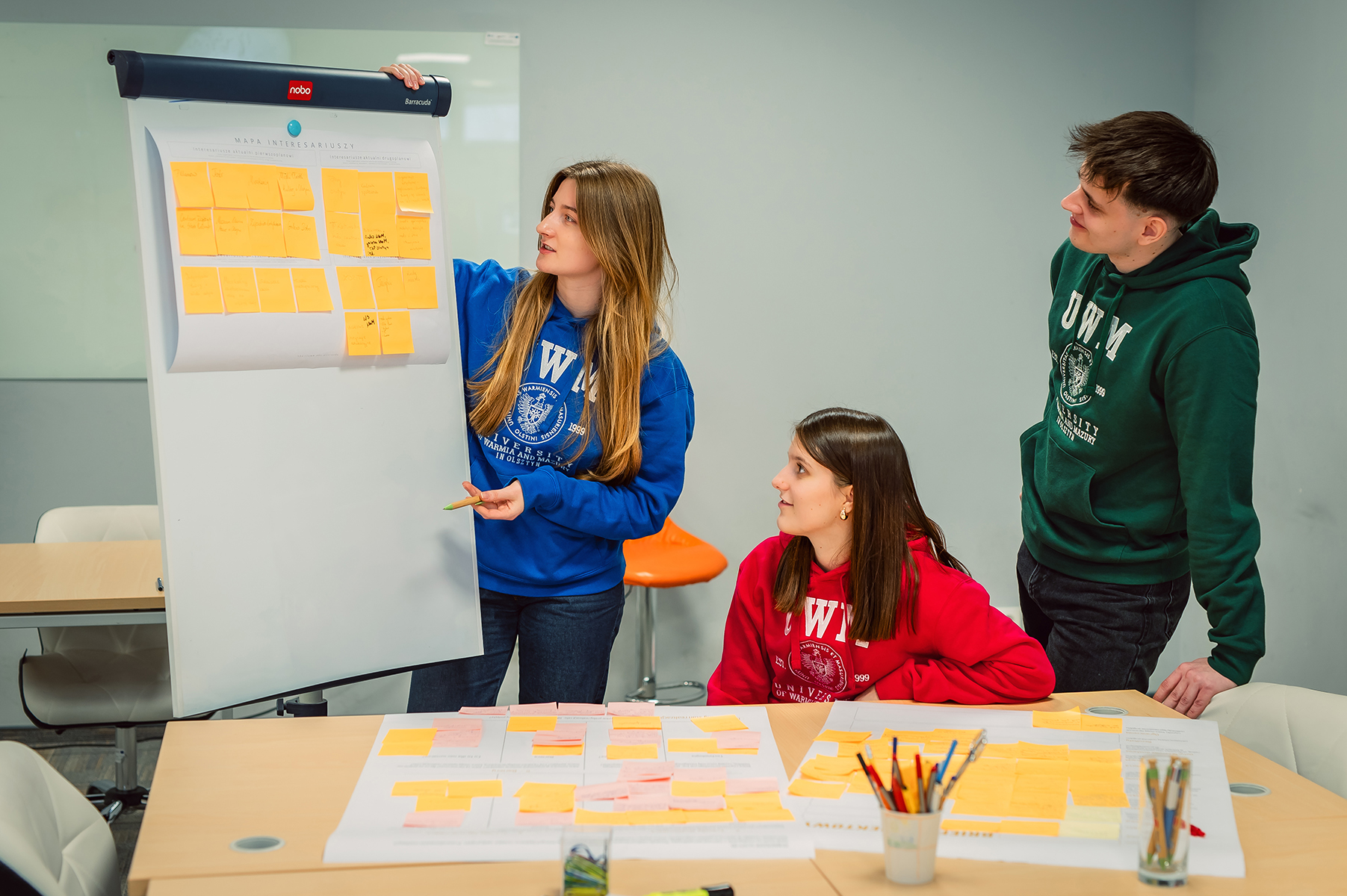 Studenci pracują przy tablicy z karteczkami podczas zajęć zespołowych
