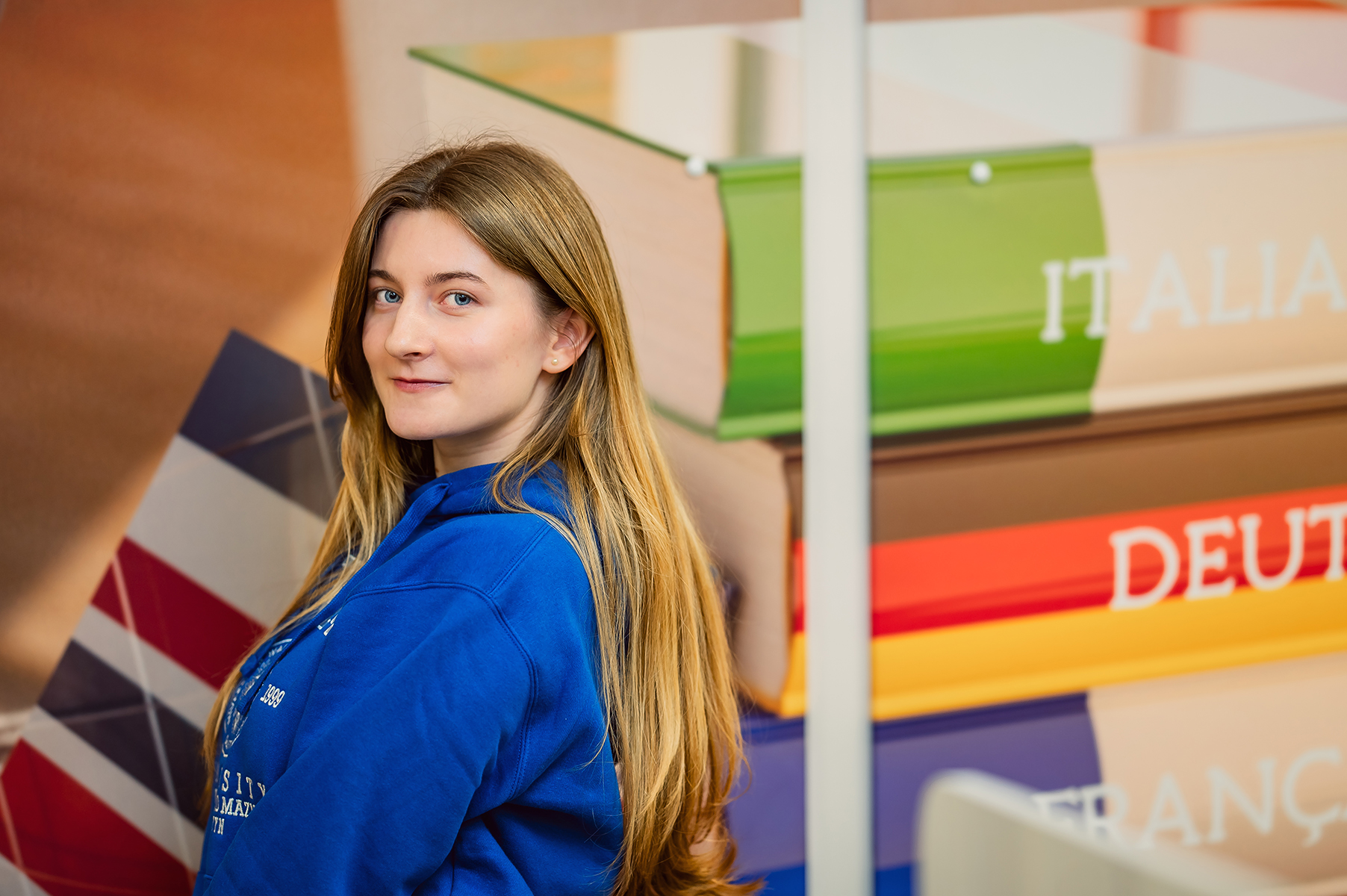 Studentka w bluzie UWM na tle dekoracji z nazwami państw i flagą brytyjską