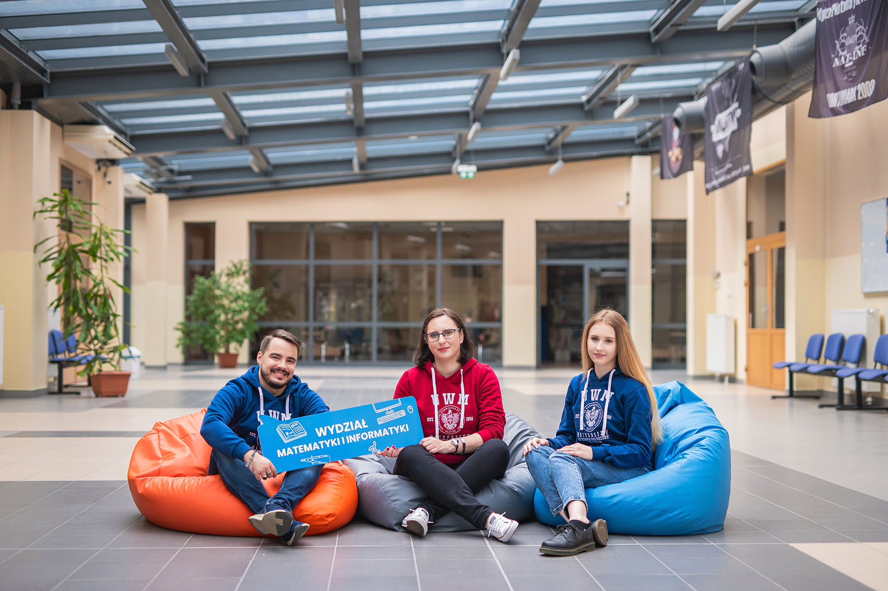 Troje studentów siedzących na kolorowych pufach sako w nowoczesnym holu wydziału