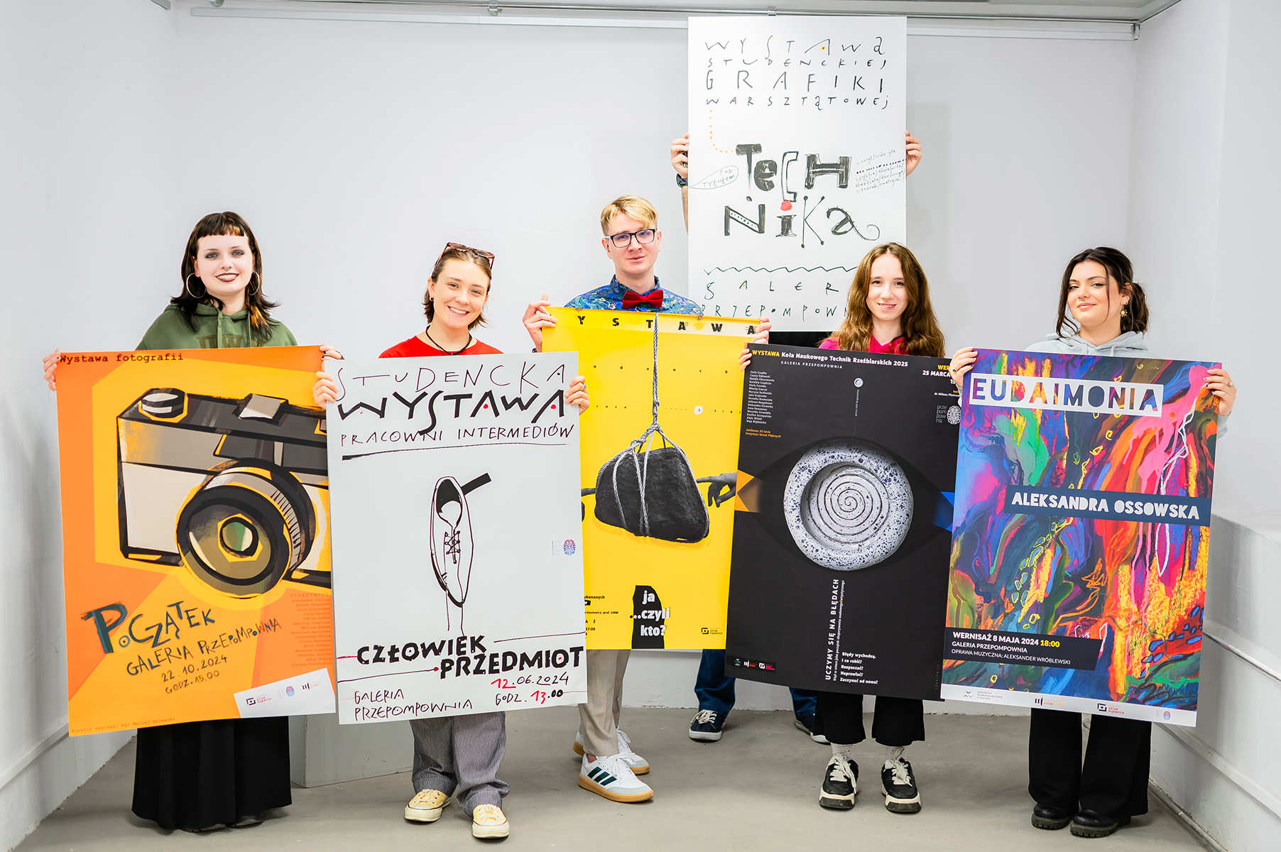 Grupa studentów stoi w galerii i prezentuje plakaty wystaw artystycznych
