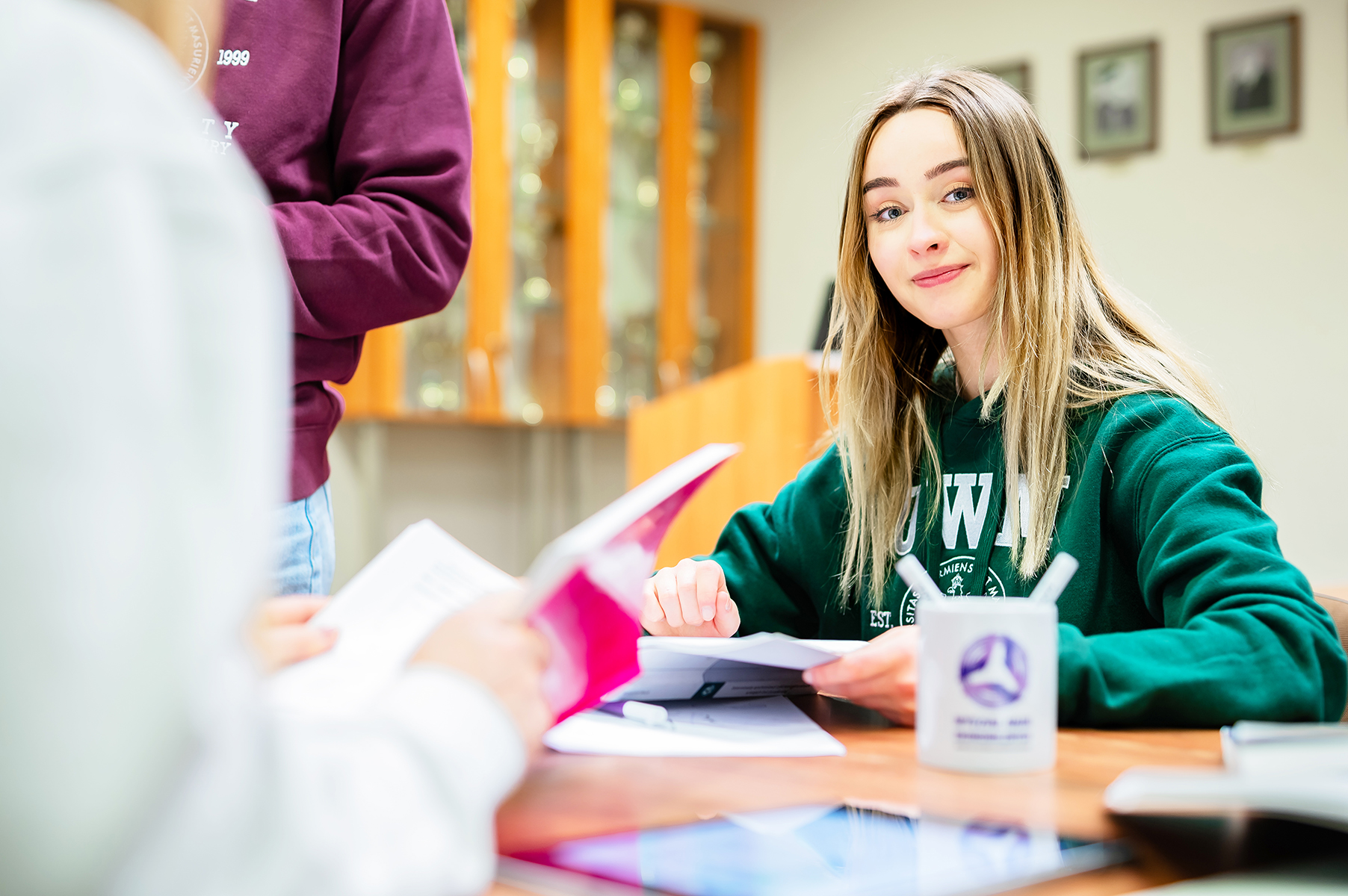 Studentka w zielonej bluzie podczas pracy grupowej przy stole z notatkami