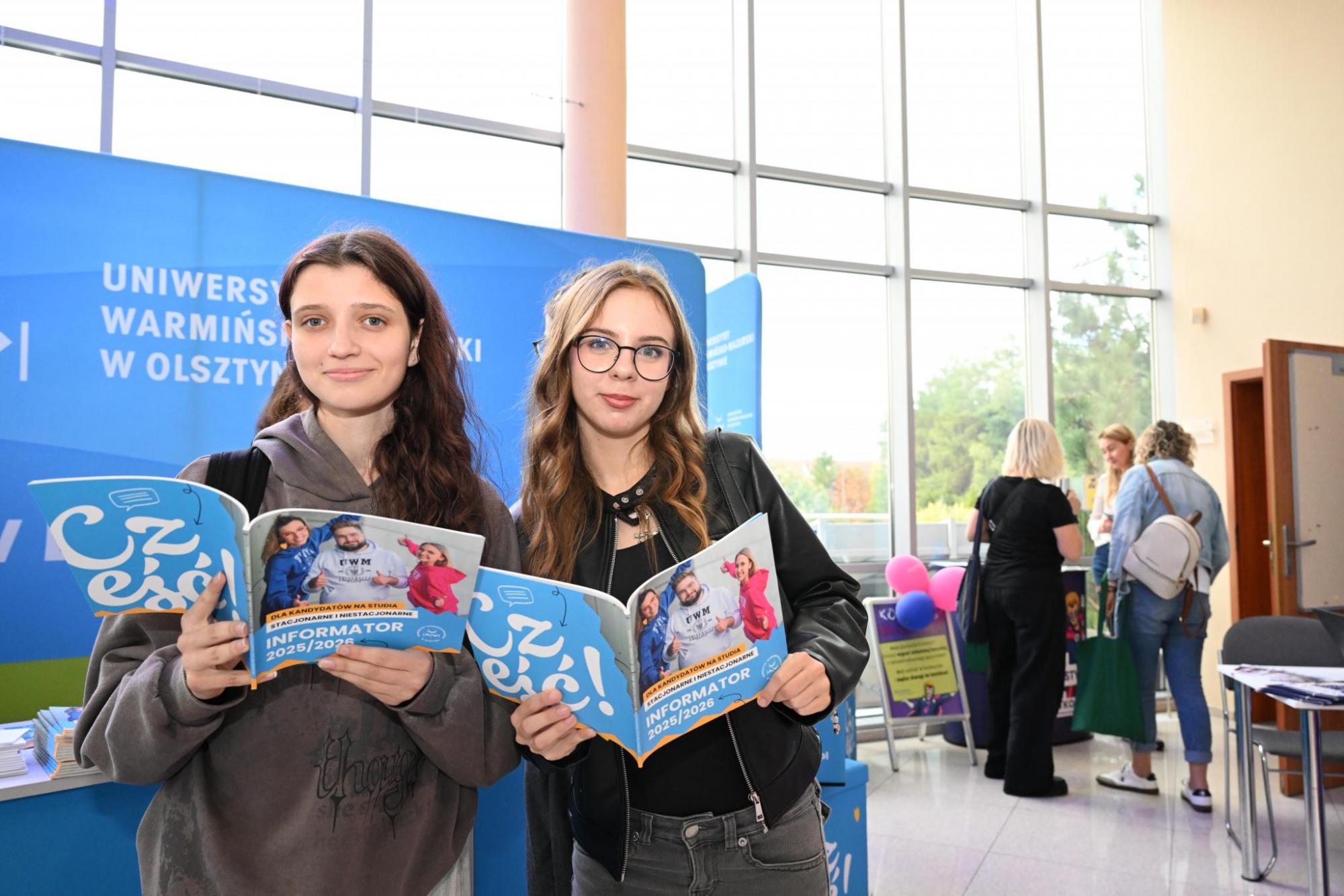 dwie osoby, trzymają informator studencki UWM